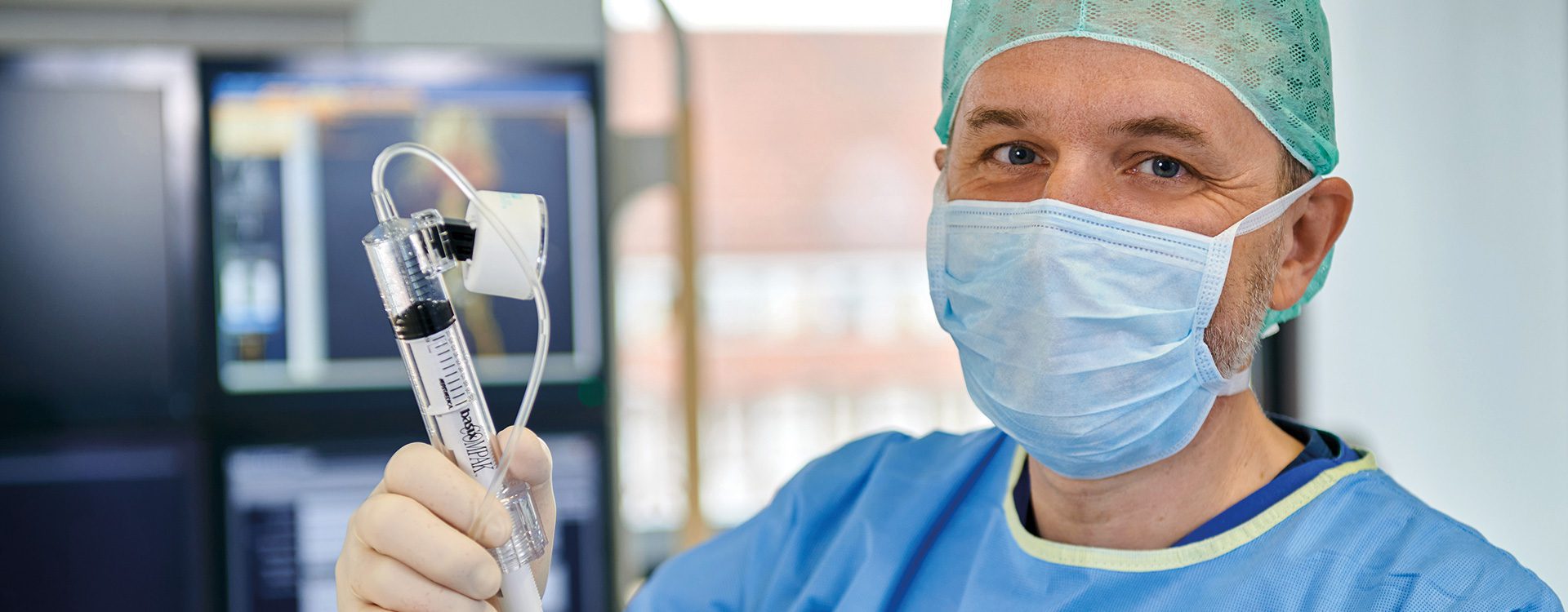 Männliche Person in blauer OP-Arbeitskleidung mit Mundschutz und OP-Haube.