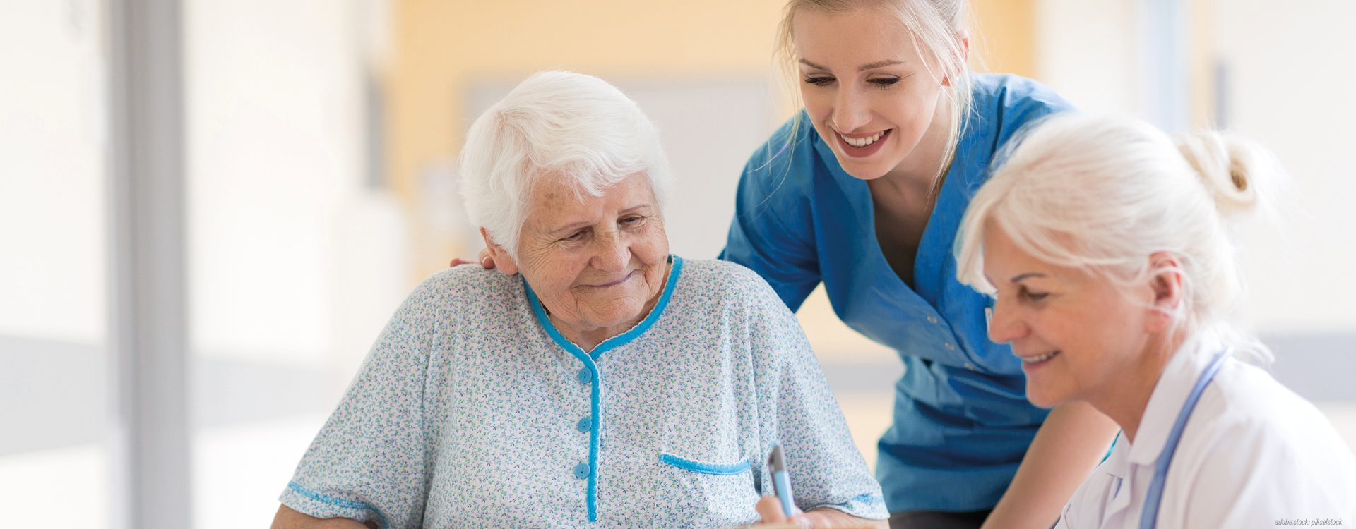 Ältere Patientin im Rollstuhl im Gespräch mit einer weiblichen Pflegekraft und einer Ärztin.