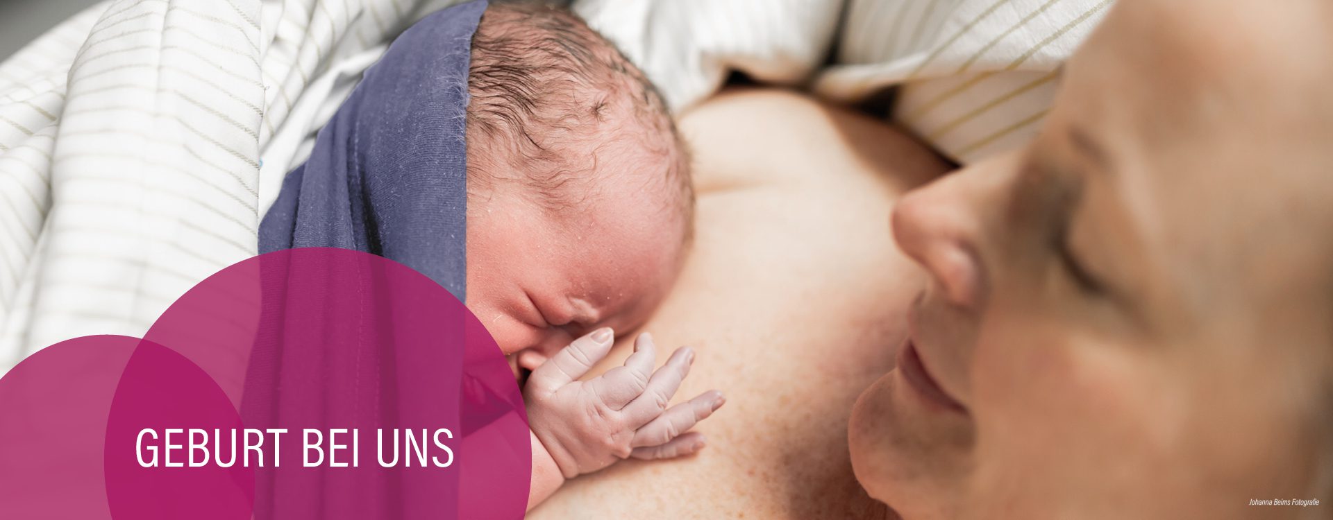 Nahaufnahme eines neugeborenen Babys mit noch feuchtem Haar, das unmittelbar nach der Geburt auf der nackten Brust der Mutter liegt und gestillt wird. Im unteren linken Bereich ist ein magentafarbenes Grafikelement mit dem weißen Text "GEBURT BEI UNS" zu sehen. Foto von Johanna Beims Fotografie.