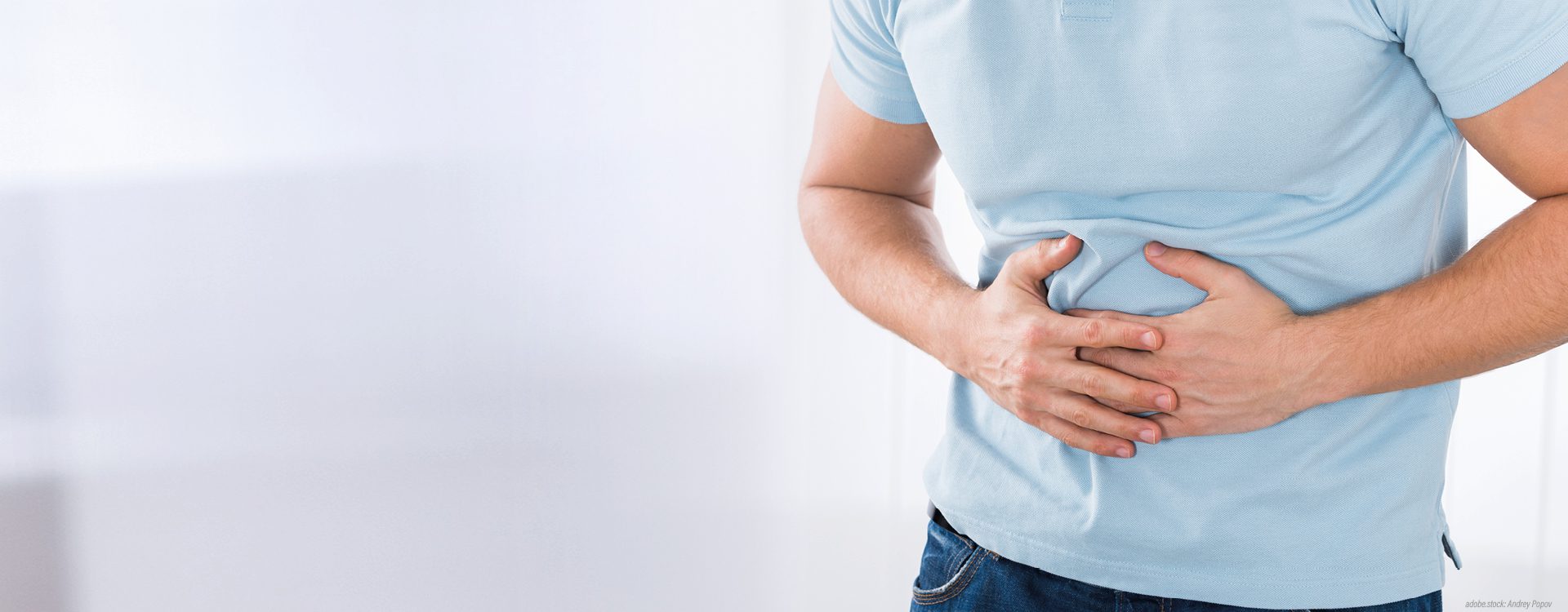 Im Ausschnitt gezeigte, männliche Person hält sich den schmerzenden Bauch.