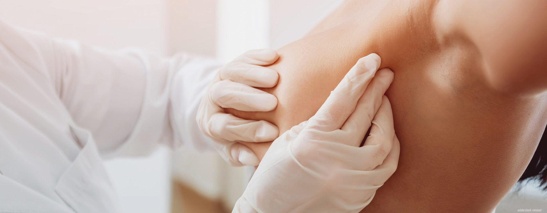 Behandschuhte Hände untersuchen eine weibliche Brust und die Achselhöhle.