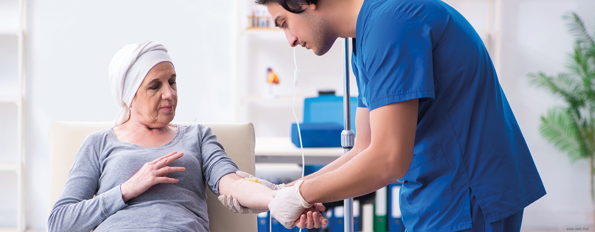 Person in blauer Krankenhausarbeitskleidung schließt einer Krebspatientin eine Infusion an
