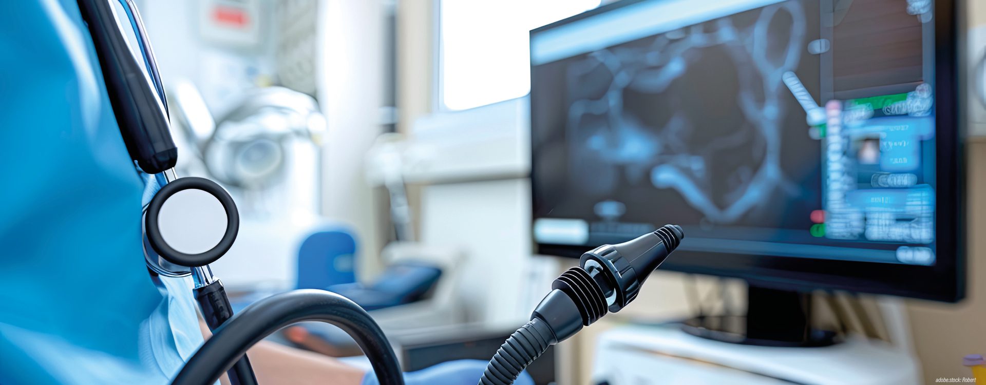 Person in bleuer Krankenhausarbeitskleidung mit Gastroskop betrachtet ein Bild am Monitor