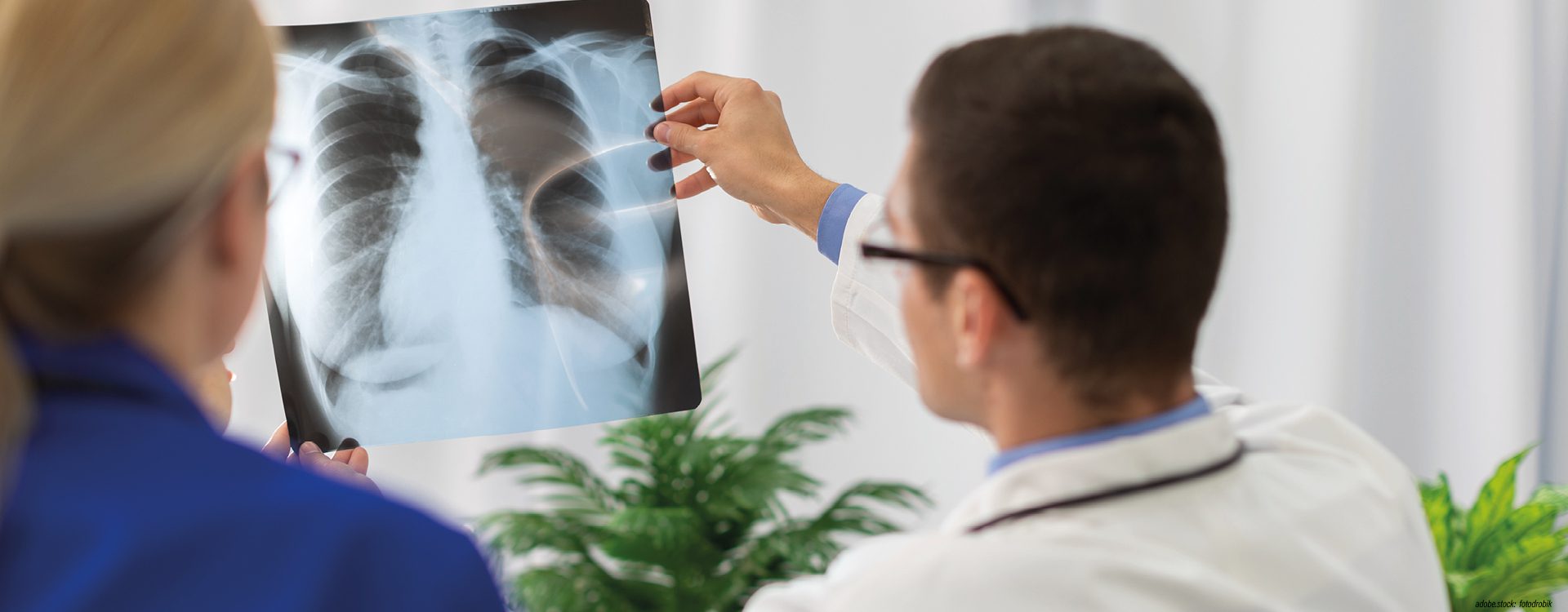 zwei Personen in Krankenhausarbeitskleidung betrachten ein Röntgenbild der menschlichen Lunge