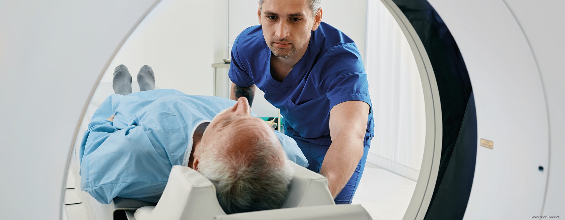 eine männliche Person wird auf einer Untersuchungsliege von einer männlichen medizinischen Fachkraft in ein Computertomographiegerät geschoben