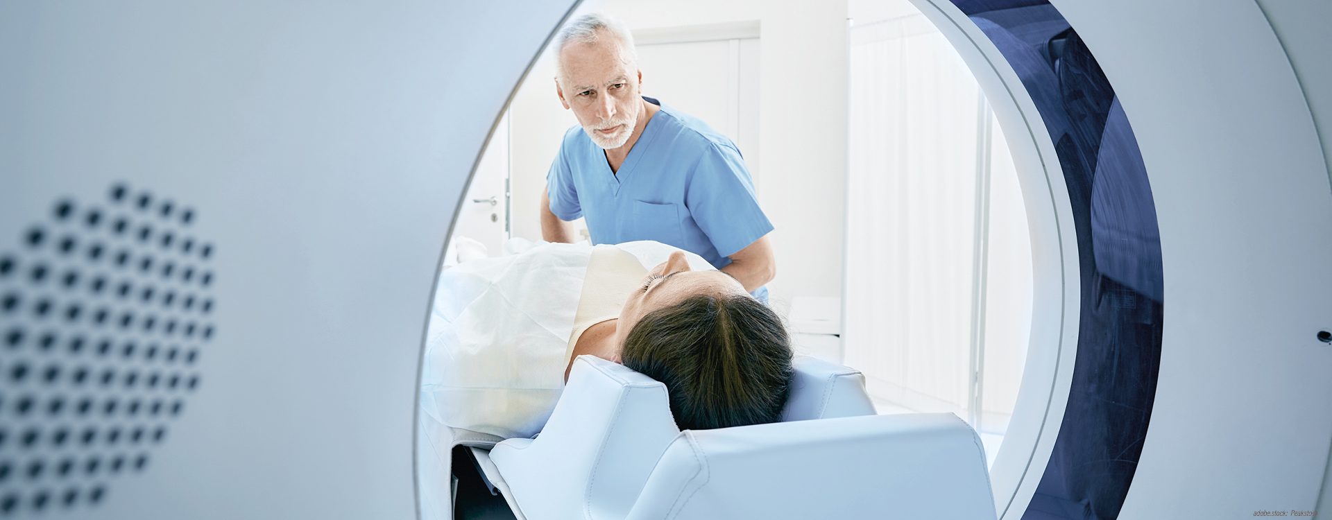 eine Person wird auf einer Untersuchungsliege von einer männlichen medizinischen Fachkraft in ein Computertomographiegerät geschoben
