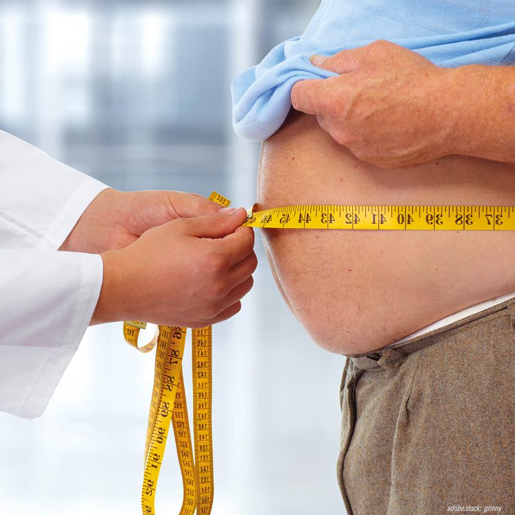Person in weißer Krankenhausarbeitskleidung misst mit einem Zentimetermaß den Bauchumfang einer männlichen Person