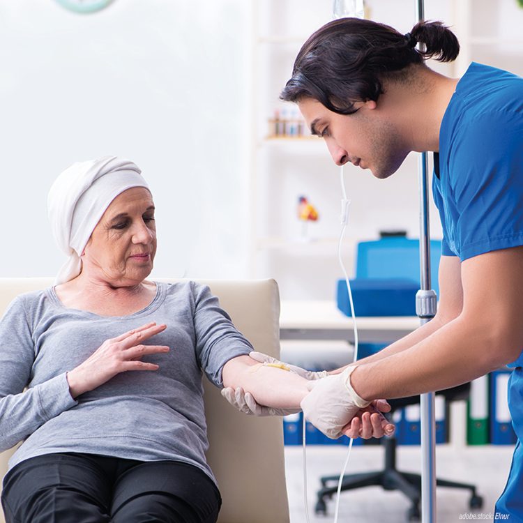 Person in bleuer Krankenhausarbeitskleidung schließt einer Krebspatientin eine Infusion an